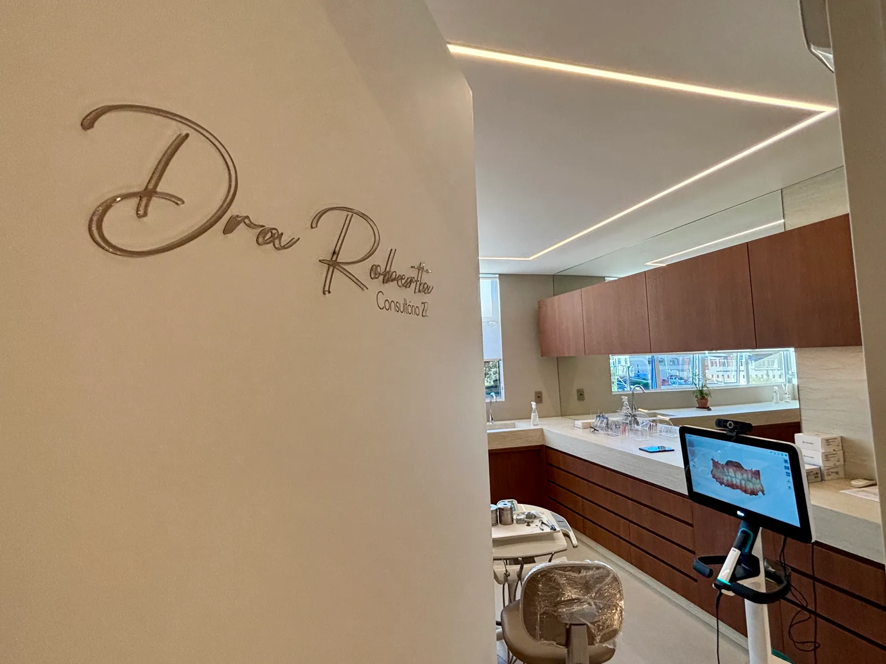 Entrada do consultório com a identificação da Dra. Roberta Gevaerd na parede e vista da sala de atendimento.