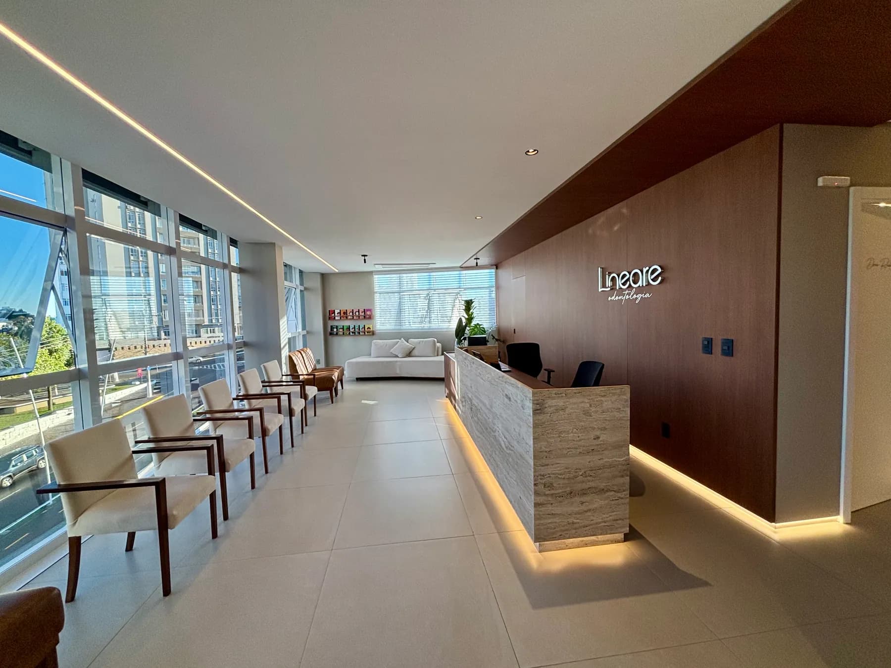 Recepção da LINEARE Odontologia, com balcão de pedra, painel de madeira e assentos junto às janelas.